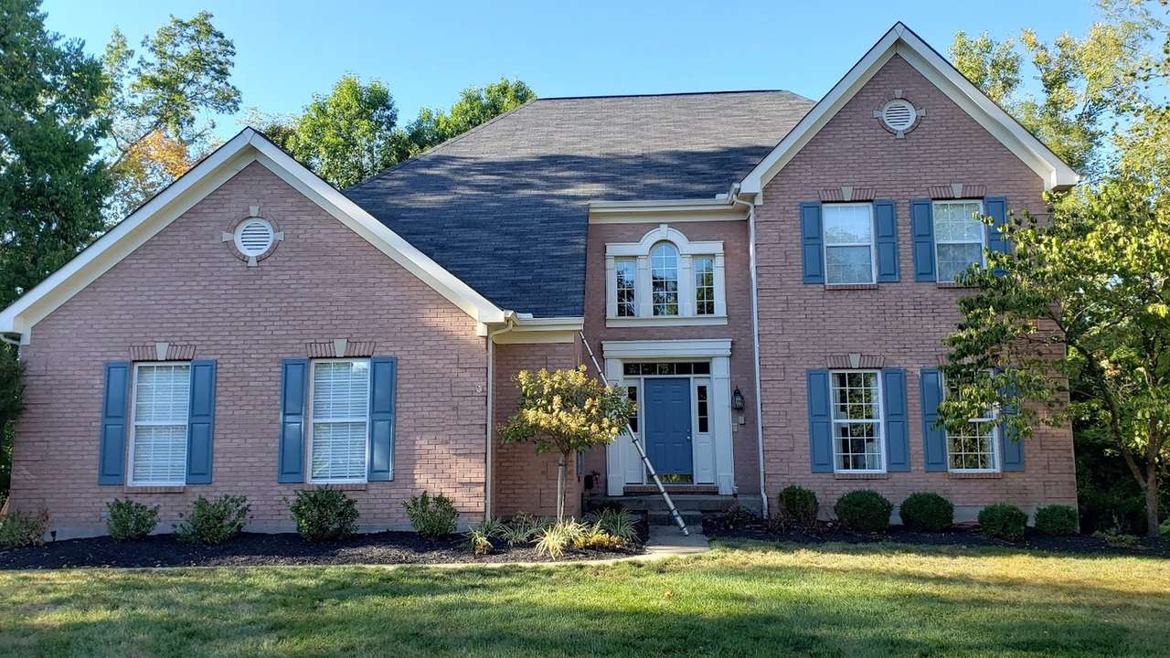 A two-story pink brick colonial house with blue shutters, a blue front door and crisp white trim, seen from the lawn on a clear day.